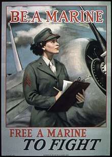 A woman member of the U.S. Marine Corps holding a clipboard and pencil, beside an airplane