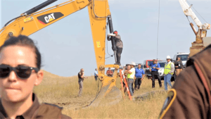 Color image of Lakota man locked down to construction equipment at direct action against Dakota Access Pipeline