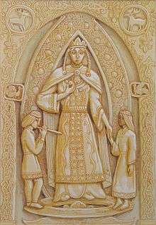 Ornately decorated artwork resembling a wood carving of a robed woman flanked by a boy and girl