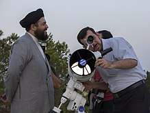 One man watches another, who looks through a modern telescope