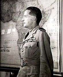 Profile half-portrait of dark-haired man in light-coloured military uniform with map of Africa in background