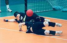 Two goalball players stretch to the left to stop the ball.