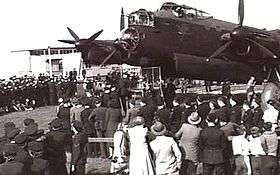 Crowd of uniformed and civilian personnel in front of four-engined military monoplane