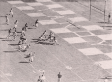 A beige image of several players in white about to run across a goal line against several players in black