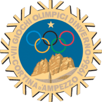 A stylized snowflake with the Olympic rings, a star and mountains. Surrounding the perimeter of the snow flake are the words, "VII Giochi Olimpici Dinverno, Cortina d'Ampezzo 1956"