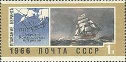On the left side of the rectangular stamp is a map of the Bering Sea showing Russia to the left and Alaska to the right, and a black line following the path of Bering's voyage which starts on the Kamchatka Peninsula, goes into the Aleutian Islands, then loops back around and ends in the Commander Islands. On the right side of the stamp is a large ship in a storm.