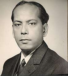 Black-and-white photo of the head and shoulders of a middle-aged man. Brown skin, receding hairline, short dark hair. He is wearing a suit and looking at the camera with a calm but determined expression.