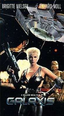 Brigitte Nielsen, holding a futuristic gun, stands in front of a spaceship