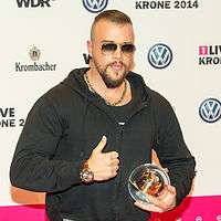 A photograph of Kollegah holding a trophy in his hands.