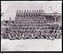 Eight rows of men in uniform with slouch hats in front of a building