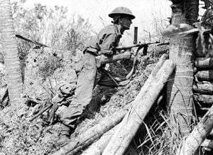 Black and white photo of a man who is wearing a military uniform and armed with a gun crouching on a step incline.