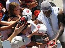 African American male in stocking cap signs autographs for fans on footballs