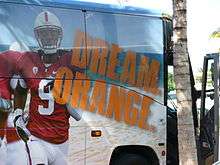 A large commercial bus is seen emblazoned with the image of a Stanford Cardinal football player and the slogan "Dream Orange".