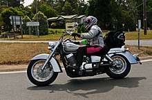 Silver cruiser motorcycle ridden on suburban road..