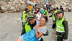 Venezuelan migrants crossing a river, aided by Colombian police