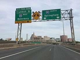 Three Highway signs with the left one saying "Exits 32A-32B, Trumbull St, I-84 West, Waterbury, Exit Only. The middle one being a sign with two arrows pointing to the two lanes. The right one says I-91 North, Springfield
