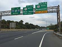 A six-lane highway at an interchange with three green signs over the road. The left sign reads east Interstate 195 to New Jersey Turnpike Interstate 95 Belmar, the middle sign reads exit 1B U.S. Route 206 north White Horse next right, and the right sign reads exit 1A U.S. Route 206 south Bordentown upper right arrow exit only.
