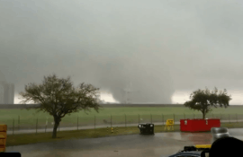 Image of tornado over the Michoud area of New Orleans with a fence and some trees visible in the foreground