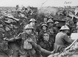 Men wearing military uniforms and helmets stand in a trench. Around them debris from battle is strewn