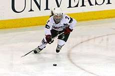 A female ice hockey player looks down at the puck as she prepares to hit it with her stick.