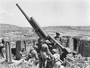Black and white photograph of several men wearing military uniforms standing next to a large artillery gun