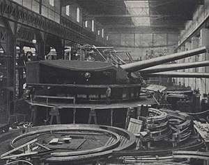 A large turret with three guns being assembled in a factory.