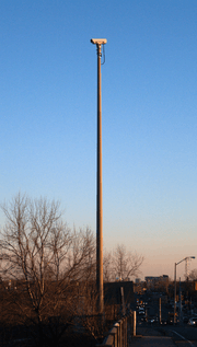 A video camera mounted on a tall pole on the side of a roadway. The camera is not pointing at the roadway visible at the bottom-right of the picture, but to the left.