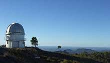 A telescope dome on a mountain-top, with a forested landscape spread out below