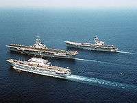 Three small aircraft carriers of different designs sailing in close formation.