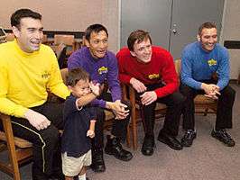 A backstage shot of four performers in bright clothes with a child.