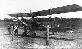 Biplane parked on landing ground, with three men standing beside it
