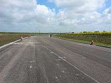 A picture of a paved, partly-complete A5758 road without any markings on its pavement and with traffic cones lining its sides