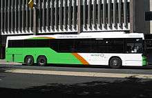 Light green, orange and white bus stopping in front of multi-story building.