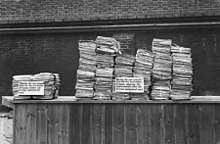 Black and white photograph of two stacks of documents on a table. The stack on the right is much larger than that on the left.