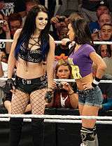 AJ Lee standing in a wrestling ring with Paige