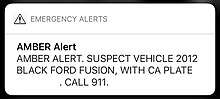 An amber alert on iOS.  Text reads in all caps "Suspect vehicle 2012 black ford fusion, with ca plate [license plate removed].  Call 911.
