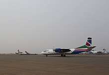 A colourful twin-engine aircraft taxiing on a dusty airport apron under a grey sky