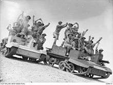Soldiers standing on two mechanised vehicles in the desert