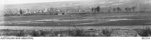 a black and white photograph of a landscape with a railway embankment in the middle distance behind which is a village
