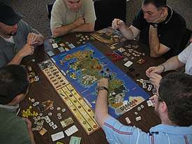 Six men seated around a table, playing the 'A Game of Thrones' board game.