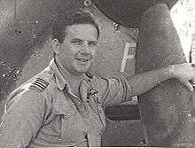 Portrait of a man in military uniform leaning one of his arms on the propeller of a plane.
