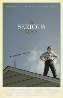 A man standing on the roof of a house, looking off to his left. His hands are on his hips. Behind him is a TV aerial.