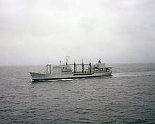A grey ship. It has three large refuelling booms midship, with black hoses.