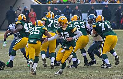 Aaron Rodgers handing the ball off to Grant, who is running toward the offensive line.