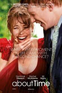 A girl in a red dress, laughing in the rain, alongside a tall red-haired man wearing a suit.
