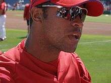 An olive-skinned young man wearing a red baseball cap and jersey and reflective sunglasses