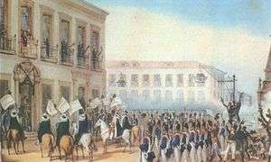 A painting depicting a semicircle of soldiers at attention and horsemen waving flags who are arranged before a large building with people standing and waving from second-story balconies