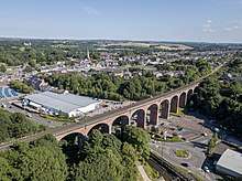 a viaduct consisting of a series of arches made of red brick, with a road passing under it and trees and a grass bank behind it