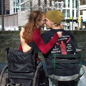 A woman in a wheelchair embracing a man in a chair