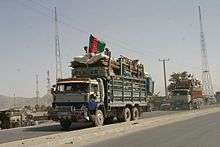 Two trucks full of household belongings, one with a black, red and green Afghan flag